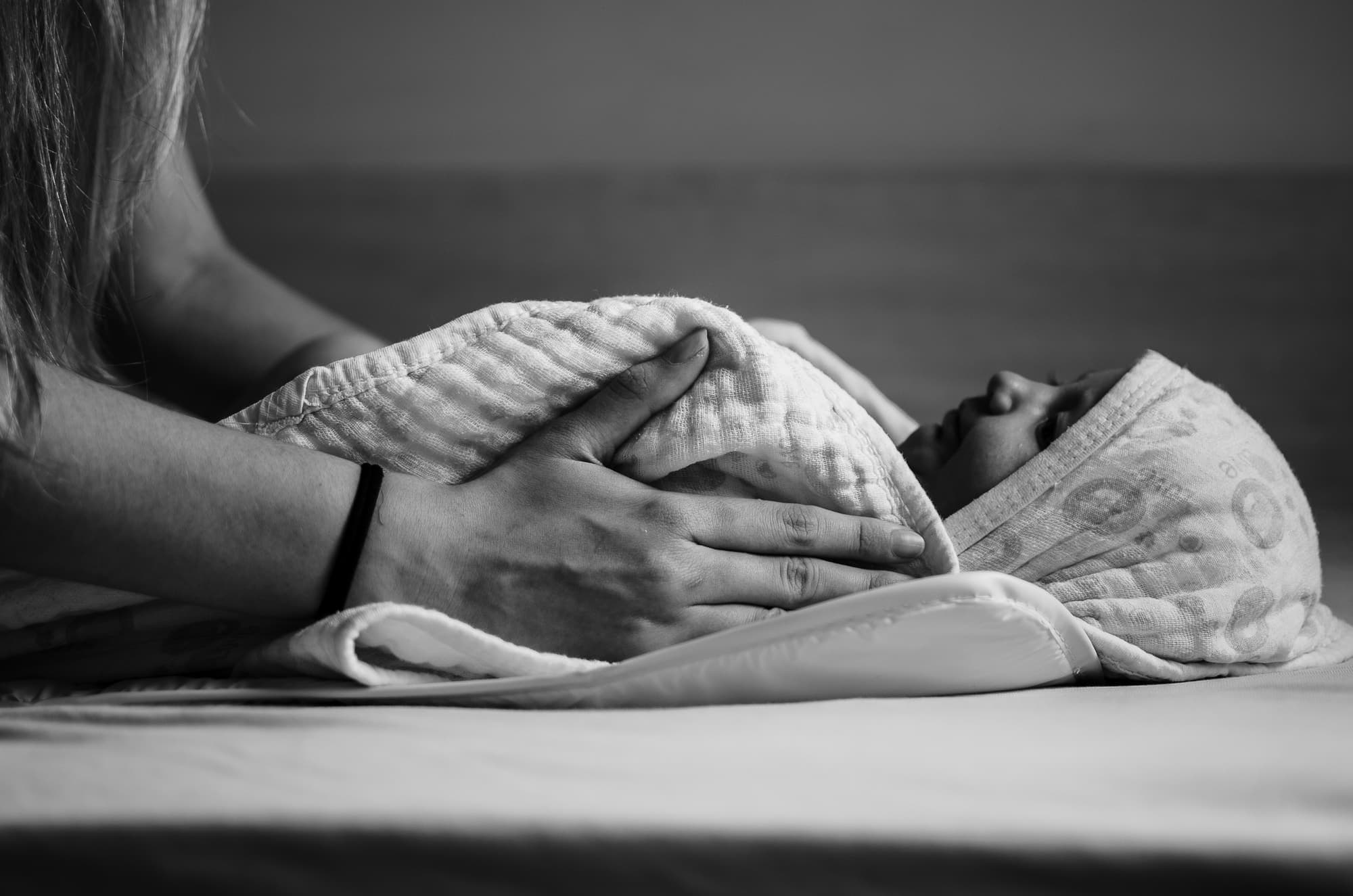 A caregiver's hands gently holding a swaddled newborn baby